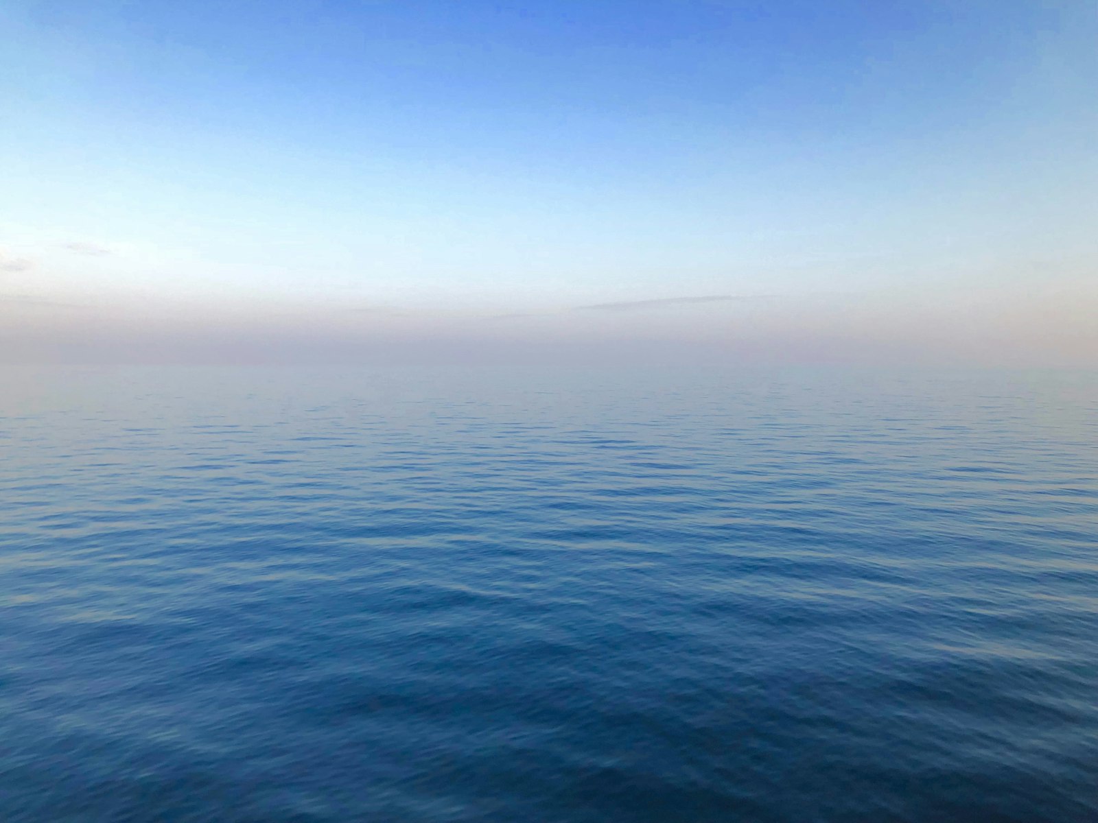 A calm, still blue ocean meeting a soft sky at the horizon